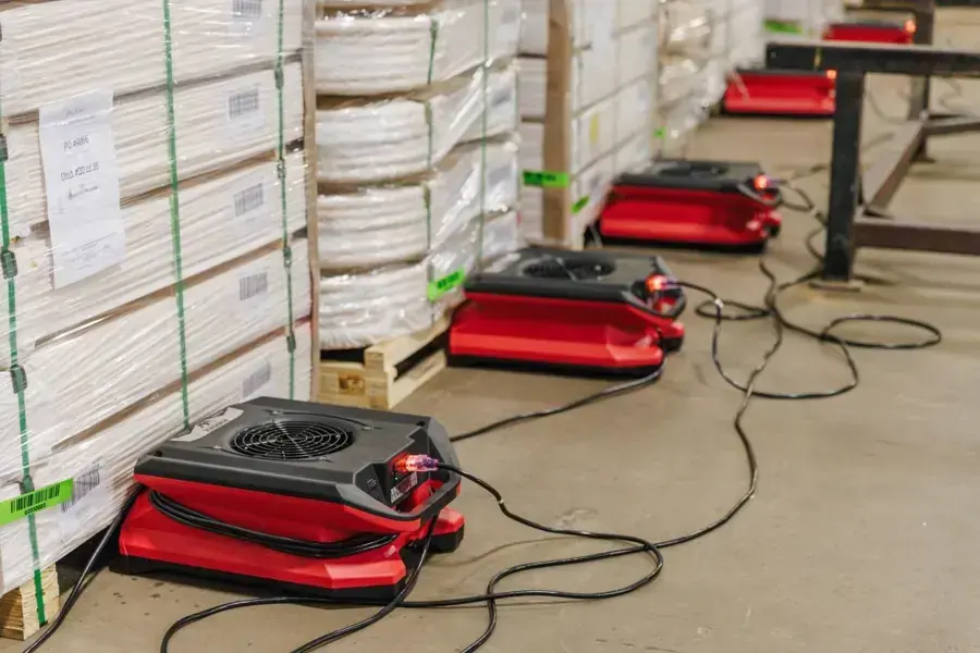 Air movers drying a warehouse floor between stacked pallets