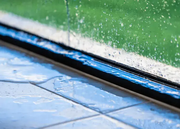 Heavy storm rain hitting a window, with water pooling in the frame